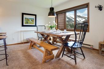 The dining area at Ranch at Steamboat RA219 features a rustic wooden table set for a meal, with a window offering views of snow-covered mountains.