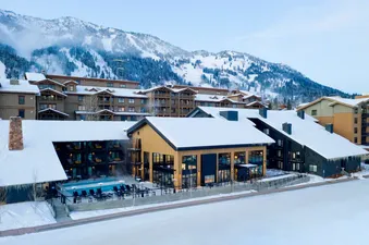 Exterior view of the snow-covered lodges and outdoor pool at Gravity Haus JH Deluxe King with a mountain backdrop.