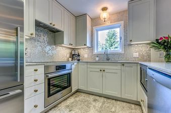 The well-lit kitchen features modern appliances, mosaic tile backsplash, and ample cabinet space.