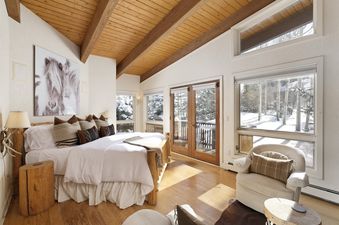 A cozy bedroom with a large bed, wooden furniture, and expansive windows offering a snowy outdoor view.