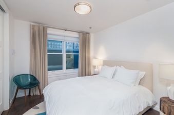 A white bedroom with a large bed, a white ceiling, and a window with white blinds.