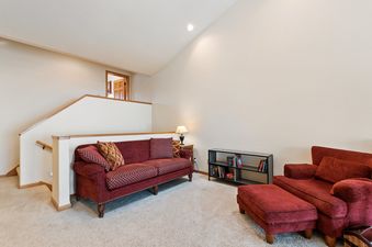 A cozy upper floor landing at Silvertip Ski Haus with a red sofa, armchair, and ottoman, featuring carpeted floors and a wooden railing.