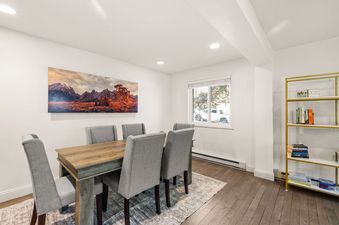 A modern dining room with a wooden table, gray chairs, mountain landscape art, and a gold bookshelf.