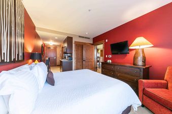 A bedroom with a king sized bed, a dresser, a lamp, and a chair.