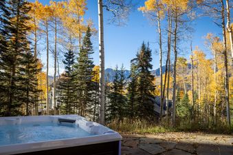 A hot tub is nestled in a vibrant autumn forest with golden aspen trees and green evergreens, offering a tranquil outdoor retreat.