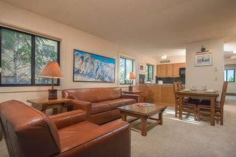 A living room in a vacation rental with a brown leather couch and armchair, a wooden coffee table and a map of a ski resort on the wall.