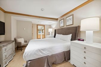 A bedroom with a king-sized bed, a dresser, and a chair with a white throw on it.