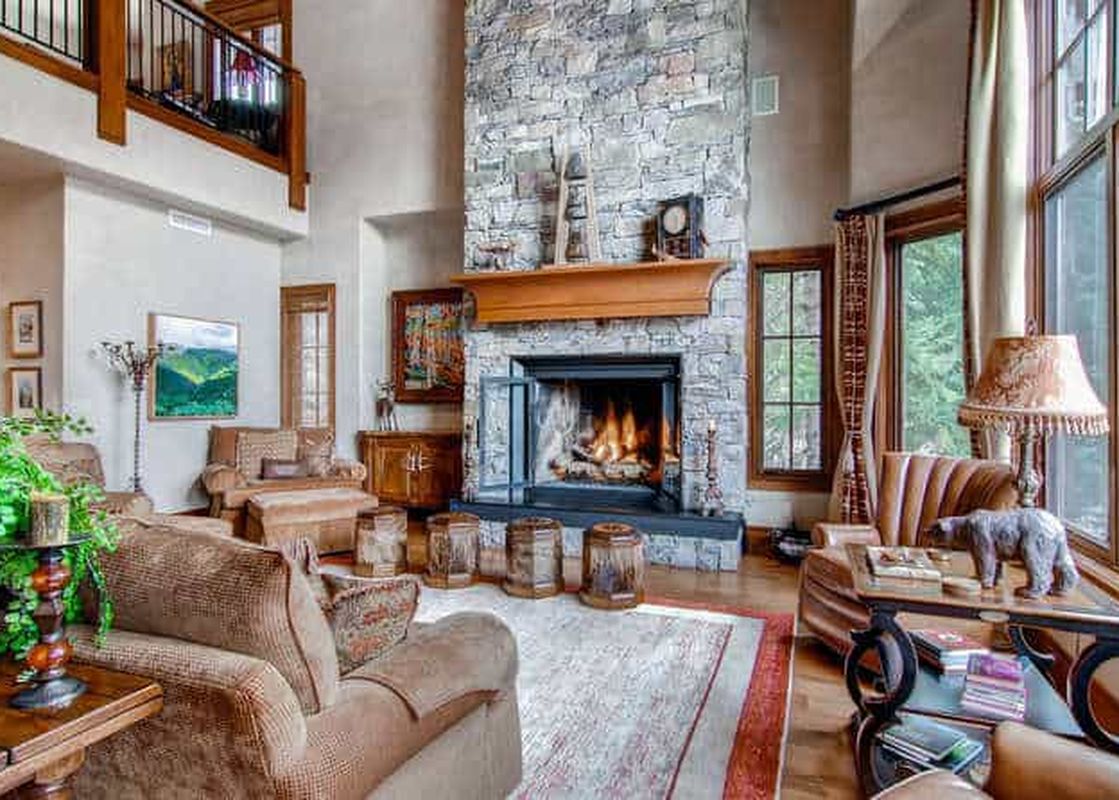 A luxurious and spacious living room with a grand stone fireplace, comfortable seating, and large windows offering views of lush greenery.