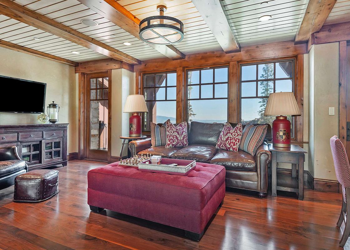 A spacious living room at Solstice at Empire Pass is furnished with a brown leather sofa and chairs, a large red ottoman with a chess set, and a flat-screen TV.