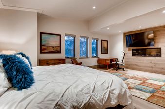 A spacious bedroom at Gondola One Chalet featuring a large bed, a work desk, a fireplace, and a television.