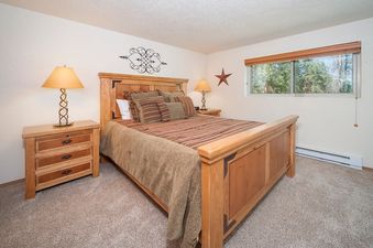 The bedroom in Beaver Village 1123 features a comfortable wooden bed frame, two bedside tables with lamps, and a large window offering a view of the surrounding trees.