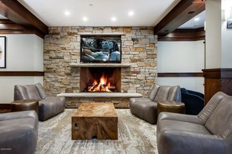 A cozy living room at Arrowleaf Lodge 107 featuring a stone fireplace with a TV mounted above, surrounded by taupe leather armchairs and a wooden coffee table.