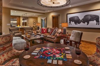 A cozy, well-lit living room features a comfortable leather couch and a game of Monopoly set up on a wooden coffee table, perfect for relaxation and entertainment.