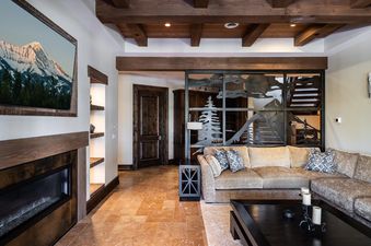 A comfortable living area at 7 Renegade Rd Moonlight Basin Lodging with a large sectional sofa, coffee table, fireplace, and a large window overlooking the mountains.