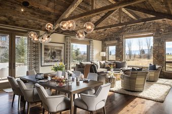Open-plan dining and living area in Four Pines 77 with rustic wood beams, a stone wall, and scenic views.
