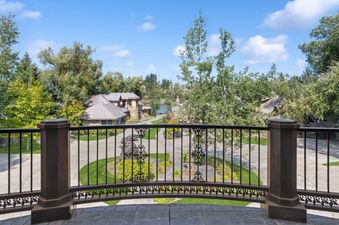 A scenic view from The Gallatin's balcony, featuring a wrought iron railing, landscaped grounds, a tranquil lake, and charming architecture under a blue sky.