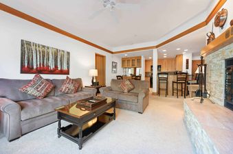 A living room with a fireplace, two couches, a coffee table, and a kitchen in the background.