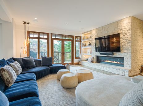 A modern and cozy living room at Snow Cloud Lodge 509 featuring a large navy sectional, a stone fireplace with a television above it, and wide windows overlooking a natural view.