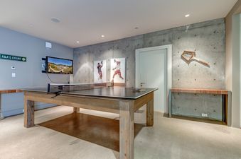 A modern games room with a ping-pong table, wall-mounted TV, and concrete and gray walls.