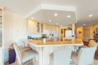 The open kitchen features a breakfast bar with stools and granite countertops, a white double-door refrigerator, and cabinets above the appliances.