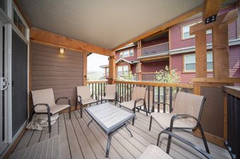 A spacious outdoor patio at Cozen Pointe I201 with comfortable seating and a dining table, offering views of the surrounding buildings and mountains.