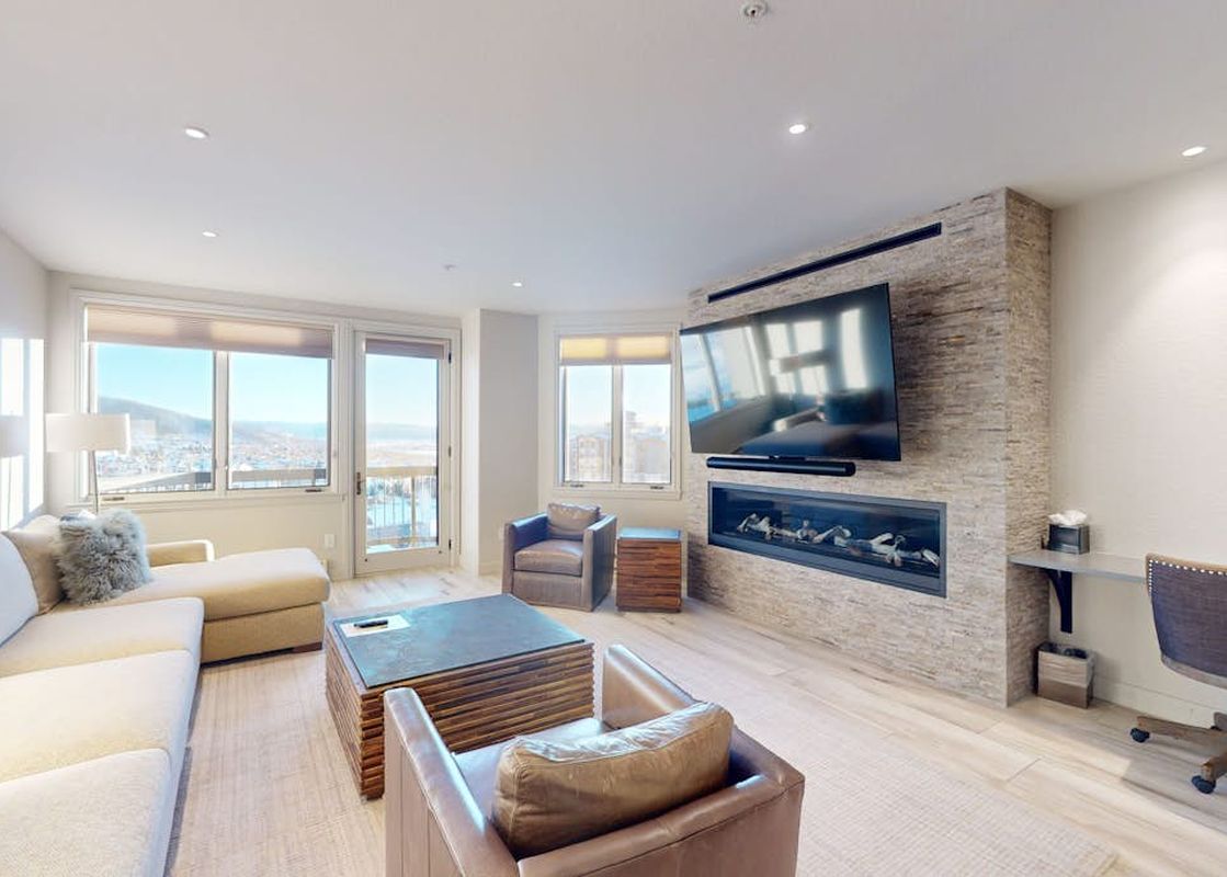 Bright and spacious living room in Torian Plum Creekside 714 featuring a stone fireplace, large television, comfortable seating, and windows with scenic views.
