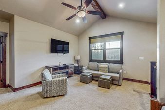 The inviting lounge area in the Keystone Townhome features a comfortable sofa, a patterned armchair, a flat-screen TV, and rustic wooden furniture, all illuminated by a ceiling fan and natural light from the large window.