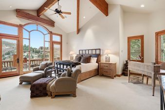 The master bedroom at Summit View Lodge at Deer Valley features a large bed, elegant wooden furniture, and expansive windows with mountain views, creating a luxurious and serene atmosphere.