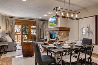 A modern dining area with a set table and an adjacent living room with a stone fireplace, TV, and outdoor view from the Town Pointe C304.