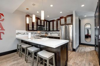 A modern kitchen with stainless steel appliances, white countertops, and a breakfast bar with four stools.