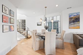 Modern open-plan dining area at Snowbound at Kings Crown featuring a round wooden table, upholstered chairs, and a stylish staircase.