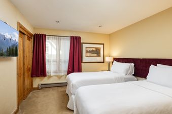 The Montaneros 417 bedroom features two beds with white bedding, a burgundy headboard, and a window with red curtains.