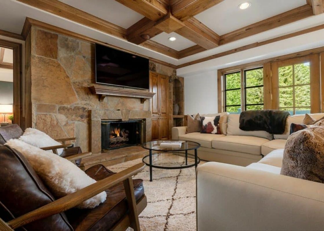 An inviting living room with a stone fireplace, a large flat-screen TV, comfortable sofas, and wooden ceiling beams at Chateau Beaver Creek Residence 210.