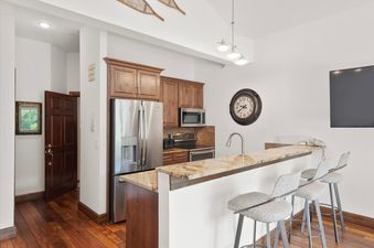 A modern kitchen in Chamonix 50 with stainless steel appliances, wooden cabinetry, and a granite breakfast bar.