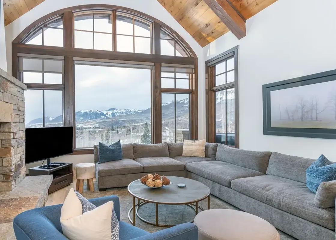 A living room with a large sectional sofa, a fireplace, and a stunning view of the mountains through a large arched window.