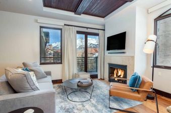 The living room of Lumiere One Bedroom Standard Residence, with a fireplace, large windows, and a view of the mountains.