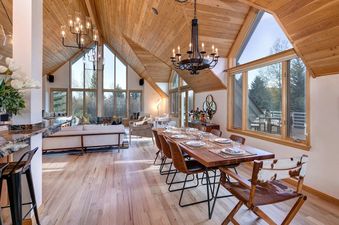 An open-plan dining and living space at Golden Spruce Jackson Hole with high wooden ceilings and large scenic windows.