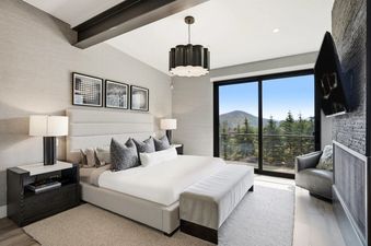 A modern and luxurious bedroom at The Ridge at Canyons Village featuring a plush king-size bed and large glass doors showing a mountain view.