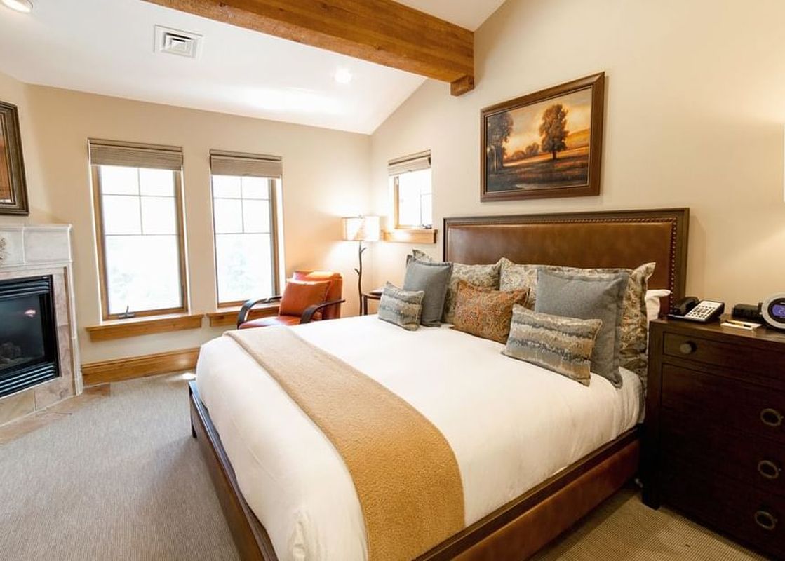 A warmly lit bedroom featuring a king bed, fireplace, and natural wood beams in The Chateaux Deluxe One Bedroom.