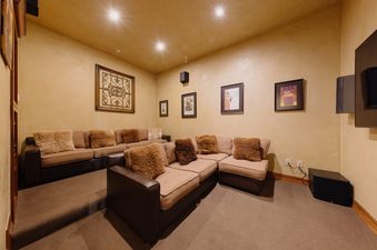 A private home cinema at Palmyra Vista Cabin at See Forever featuring tiered seating and plush brown couches with fluffy pillows, set against warm-toned walls with subtle decor and soft lighting.
