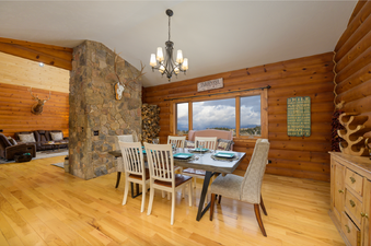 The dining area at 2665 Golden Eagle Drive features a rustic wooden table with six chairs, a large window offering mountain views, and log cabin-style walls.