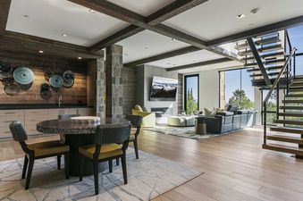The living area of Moonshadow 8927, featuring a dining table, a lounge, a bar, and a staircase with a large window.