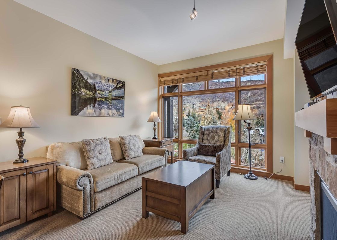 The living room of Capitol Peak Lodge 3207 features a comfortable couch and a large window with a view of the mountains.