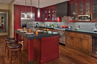A modern kitchen with deep red cabinetry, stainless steel appliances, and a central island with bar stools.