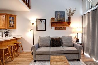 A cozy living and dining area at Snowcrest 300 featuring a gray sofa, a wooden coffee table, a breakfast bar with stools, and rustic decor.