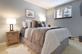 A cozy bedroom with a large bed, two nightstands with lamps, and a window revealing a snowy outdoor scene.