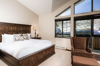 A cozy bedroom with a large wooden bed and a comfortable chair, offering a view of a snow-covered landscape.
