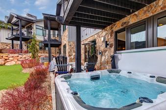 A private hot tub on a patio outside the Frost Haven, surrounded by landscaping, with the multi-story building in the background.