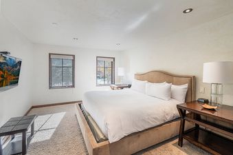 A bedroom with a king-sized bed, a television on the wall, and a window with a view of trees.
