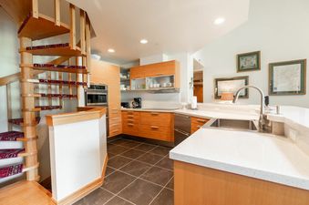 A modern kitchen with light wood cabinets, dark tiled floors, and a white countertop with a sink is shown.